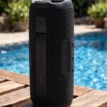 JBL Flip 7 portable Bluetooth speaker in black with fabric finish standing upright on a wooden poolside table